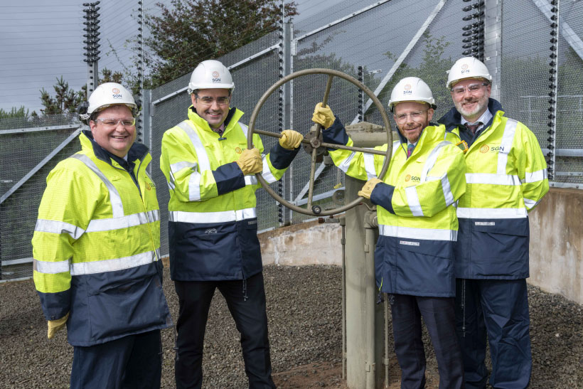 Four men wearing high-vis and hard hats holding a valve to commission a gas pipeline.