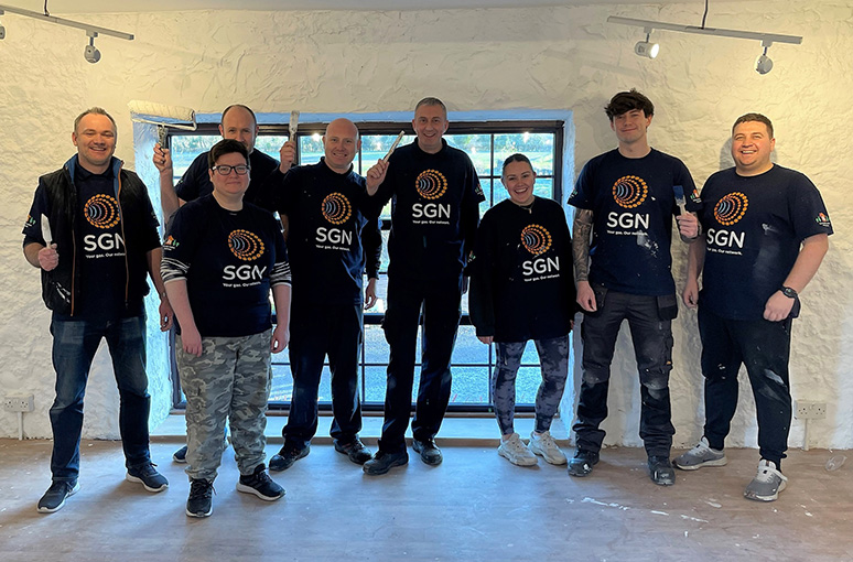 A team of people holding paintbrushes, standing in an empty building