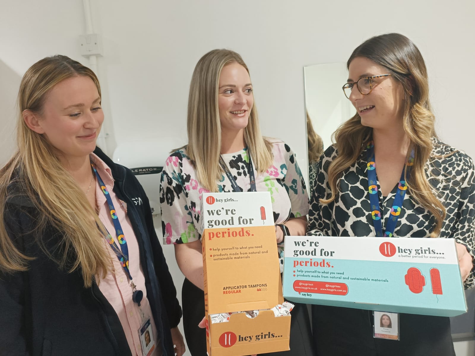 Three women holding boxes of Hey Girls period products