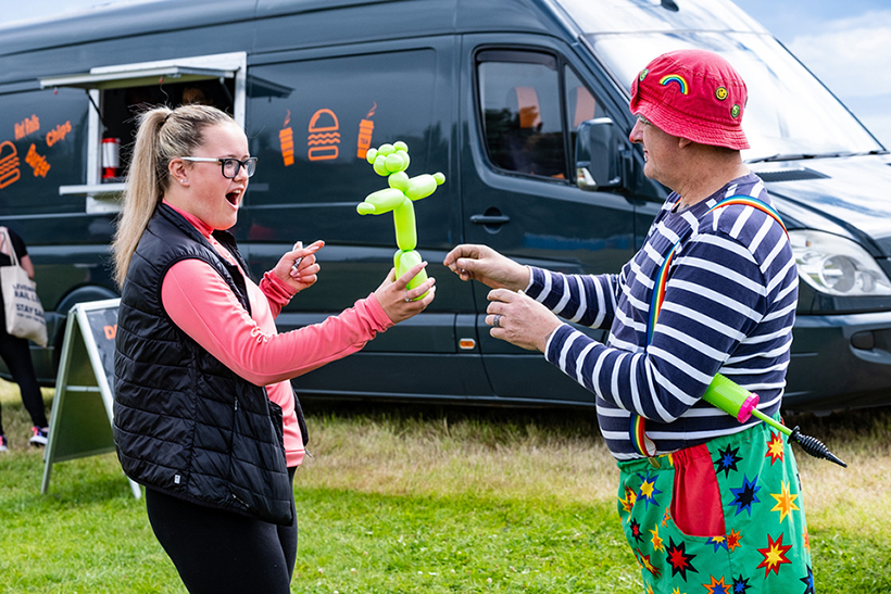 A man dressed as clown hands a young person a balloon model