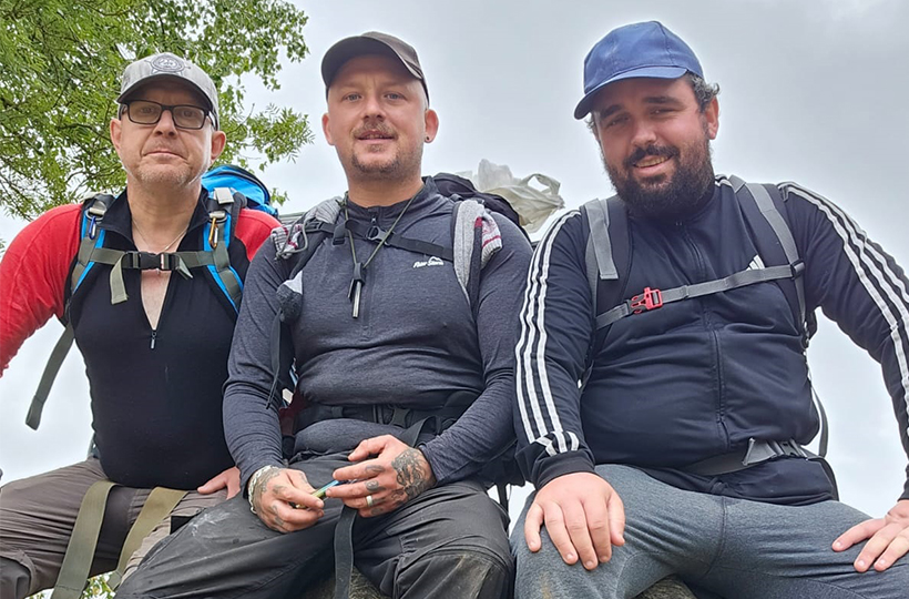 Three men in walking gear sitting and looking to camera