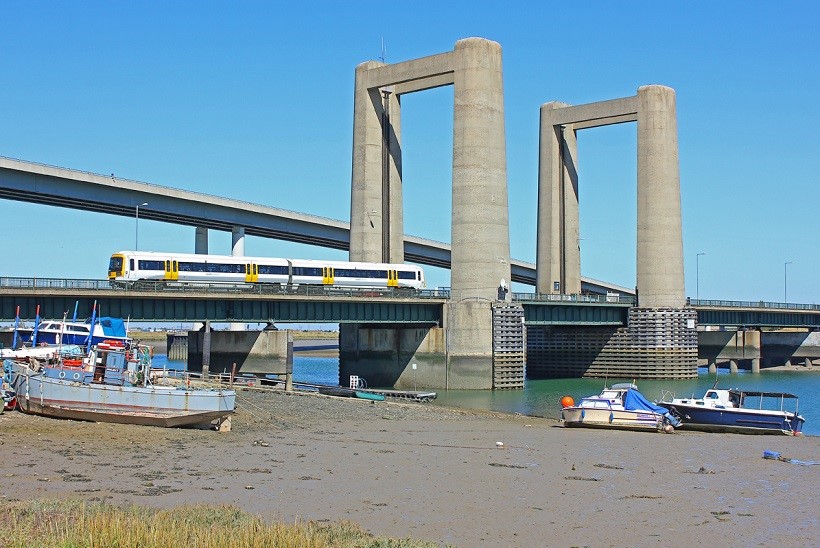 Establishing shot of Kingsferry Bridge with train travelling over the bridge. Boats and River Swale also pictured in the foreground.