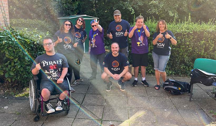 A group of adults in SGN t-shirts with young adults with learning disabilities, all giving thumbs up