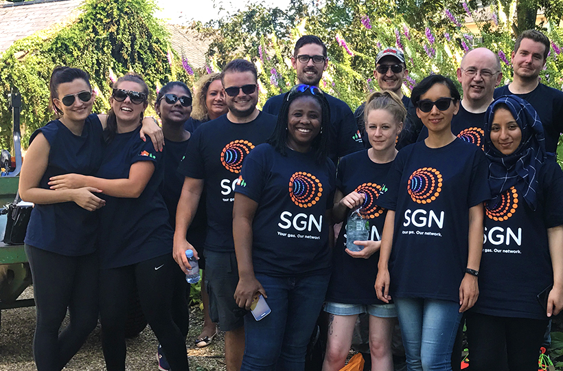 A group of 15 people wearing SGN branded T-shirts standing in a park. They are smiling and look relaxed.