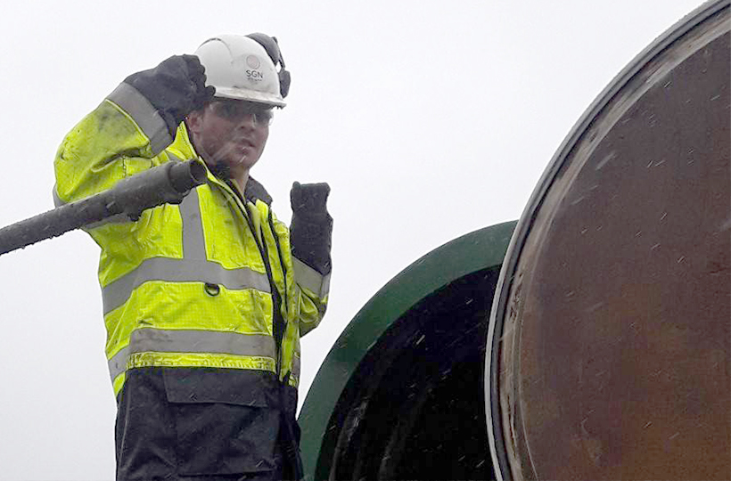 A young man in SGN PPE stood in the rain next to a pipe