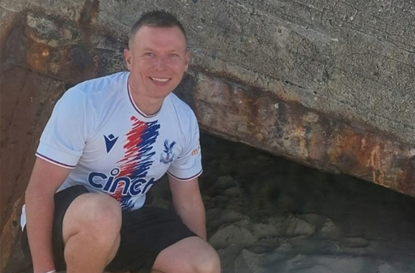 A smiling man crouching next to some rocks