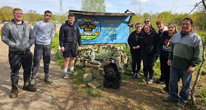 Nine people in coats and tshirts smiling in front of a sign for Happy Pants Ranch with a turkey