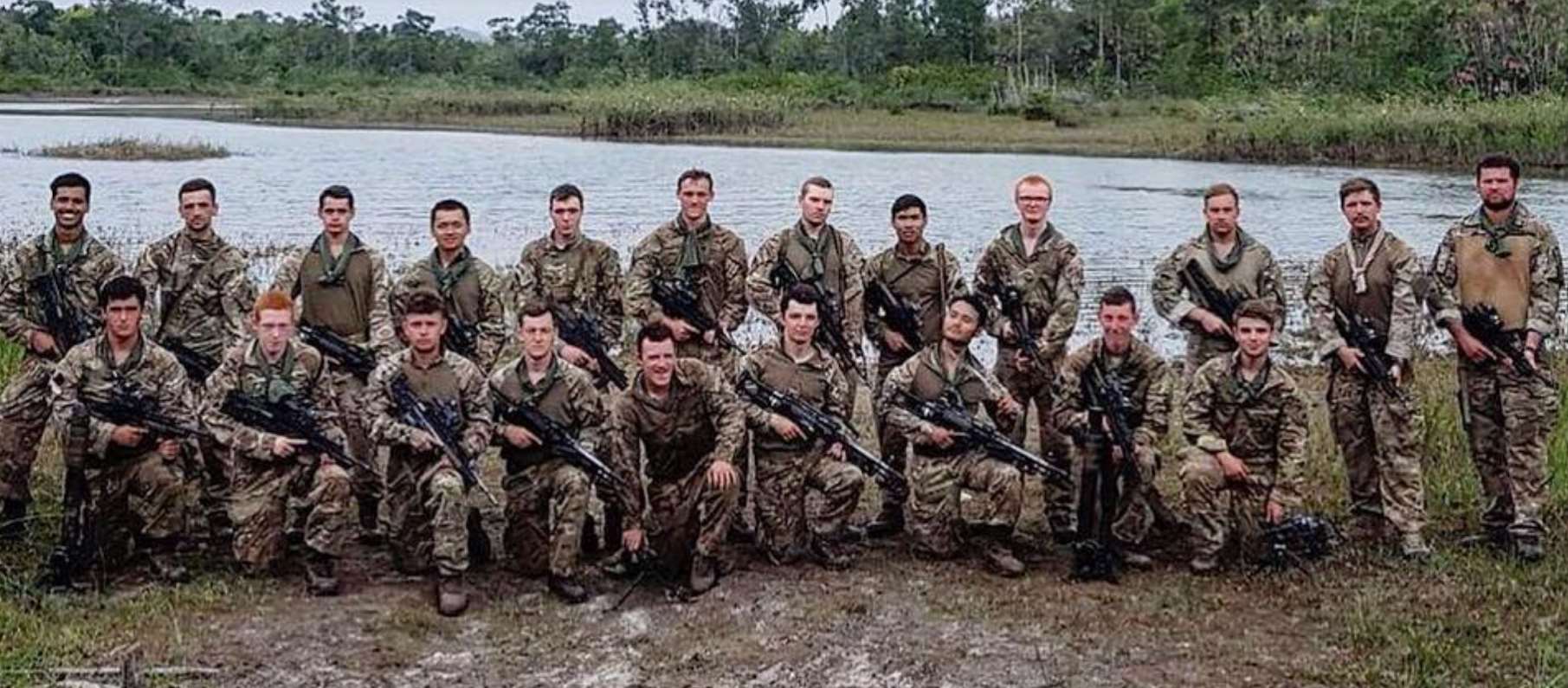 A large group of young men in army fatigues holding guns next to a lake