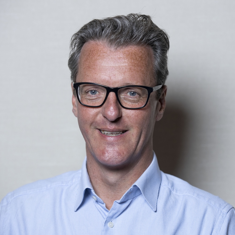 A man with grey hair and glasses wearing a pale blue shirt