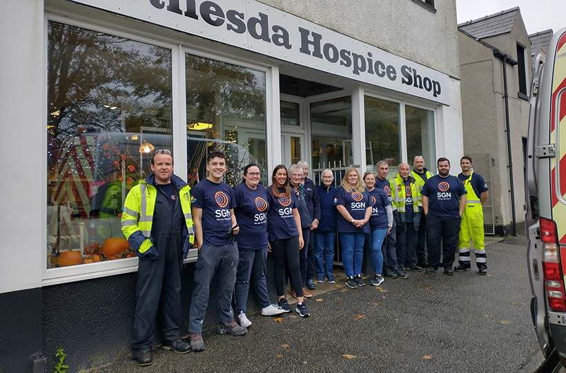 A large group of people outside a hospice shop in a street