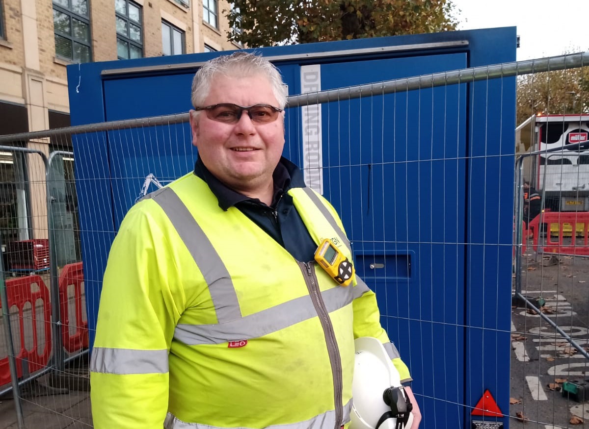 Head and shoulders image of man in his 50s with grey hair. He is facing the camera and wearing personal protective equipment