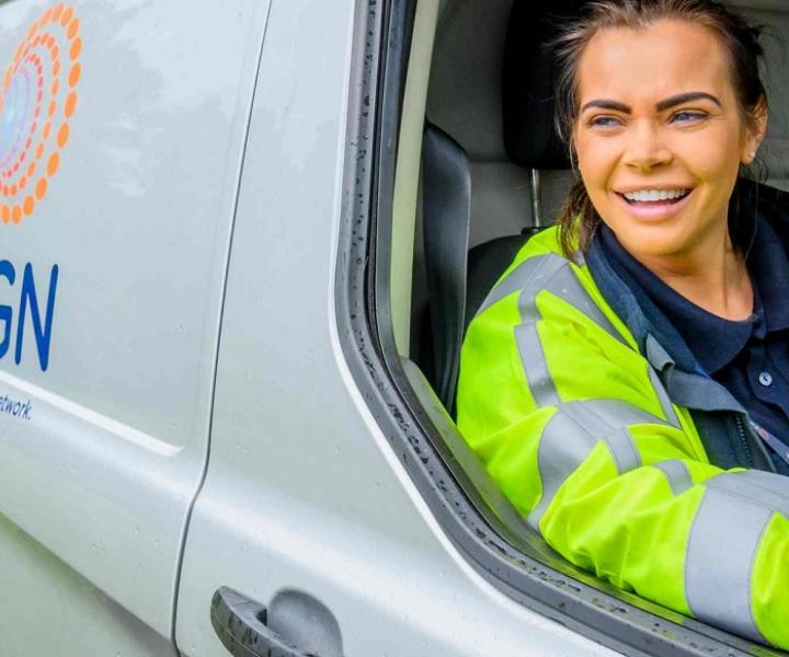 An engineer sitting in an SGN van. She is wearing a hi-vis vest and smiling.