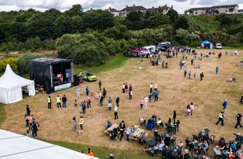 Drone view of a crowd of people gathered in park, with a marquees, tents and a stage