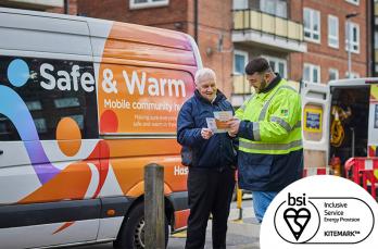 An SGN engineer talking with an older man in front of an SGN Safe & Warm van, parked on a council estate. BSI Kitemark is displayed in the corner.