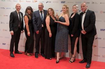 Seven people on a red carpet with Hannah Moseley-Brown in the middle, holding her glass award